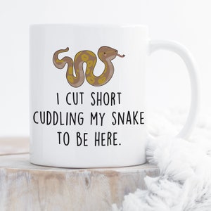 May include: White ceramic mug with a cartoon snake and the text "I cut short cuddling my snake to be here."