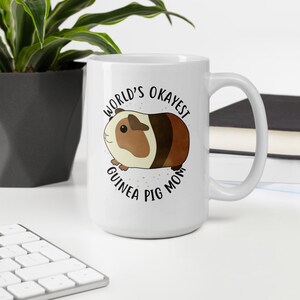 May include: White ceramic mug with a brown and white guinea pig illustration and the text "World's Okayest Guinea Pig Mom".