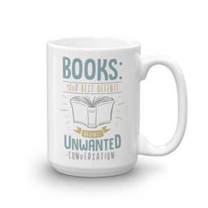 Puede incluir: Taza de cer&aacute;mica blanca con el texto "BOOKS: YOUR BEST DEFENSE AGAINST UNWANTED CONVERSATION" en verde azulado y dorado. El dise&ntilde;o incluye una ilustraci&oacute;n de un libro abierto. La taza tiene un asa grande.