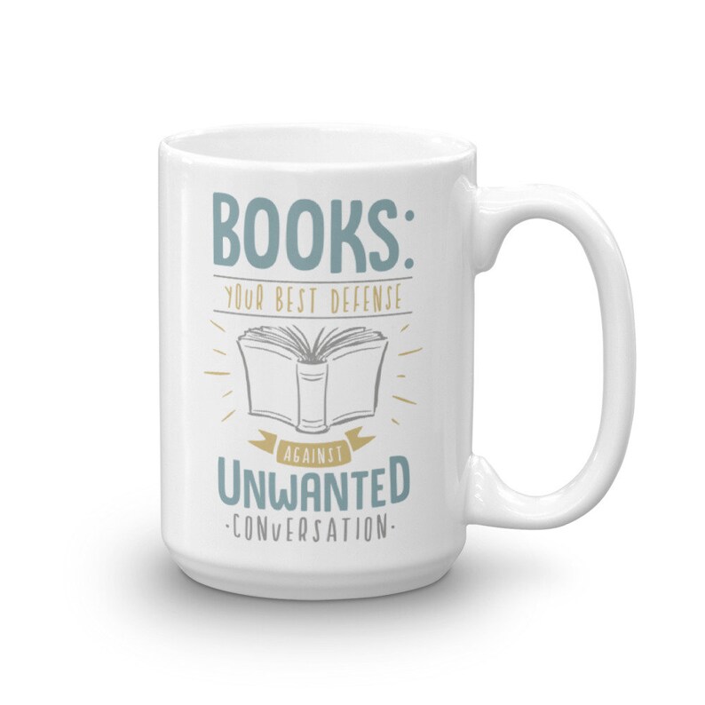 Puede incluir: Taza de cer&aacute;mica blanca con el texto "BOOKS: YOUR BEST DEFENSE AGAINST UNWANTED CONVERSATION" en verde azulado y dorado. El dise&ntilde;o incluye una ilustraci&oacute;n de un libro abierto. La taza tiene un asa grande.