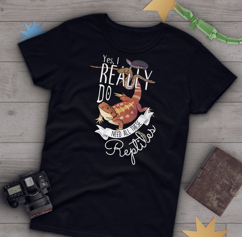 Puede incluir: Camiseta negra con un gr&aacute;fico blanco de un drag&oacute;n barbudo, una serpiente y una tortuga. El texto en la camiseta dice "S&iacute;, realmente necesito todos estos reptiles."