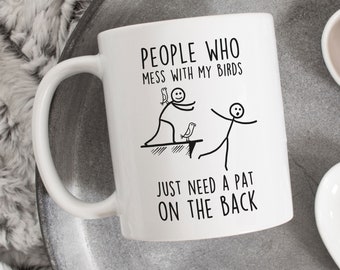 May include: White ceramic mug with a black design. The mug says "People who mess with my birds just need a pat on the back". The design includes a stick figure with two birds on its back and another stick figure running away.