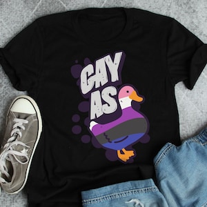 May include: Black t-shirt with a cartoon duck and the text "Gay as" in white and purple lettering.