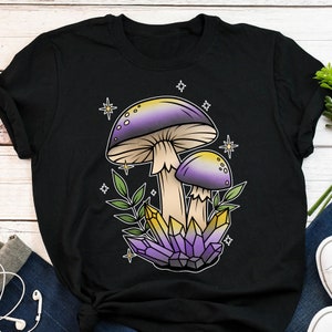 Puede incluir: Camiseta negra con un gráfico de dos setas moradas y amarillas con cristales y estrellas.