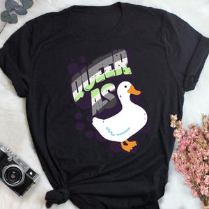 May include: Black t-shirt with a white goose and the text "Queer as" in green, purple, and black.