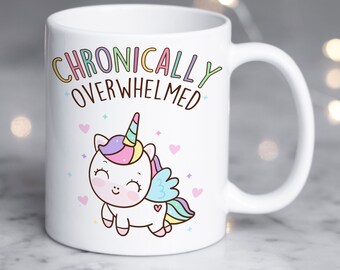 May include: White ceramic mug with a rainbow unicorn illustration and the text "Chronically Overwhelmed".