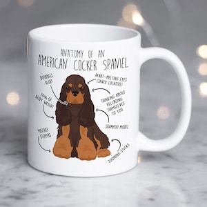 May include: White ceramic mug featuring a brown and tan American Cocker Spaniel illustration with humorous anatomical labels. Text includes "Anatomy of an American Cocker Spaniel", "Doorbell Alert", and "Heart-Melting Eyes".