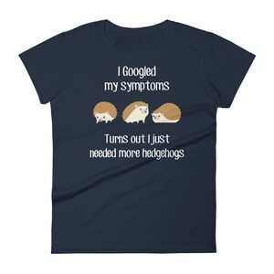 May include: A navy blue t-shirt with white text that reads "I Googled my symptoms Turns out I just needed more hedgehogs". Three cartoon hedgehogs are pictured below the text.