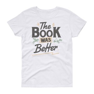 Pode incluir: Camiseta branca com um gr&aacute;fico preto que diz "The Book Was Better" com um unic&oacute;rnio e um drag&atilde;o de cada lado do texto.