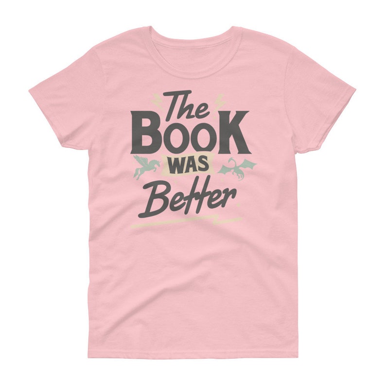 Pode incluir: Camiseta rosa para mulher com o texto "The Book Was Better" em preto. Um pequeno drag&atilde;o verde e um unic&oacute;rnio branco est&atilde;o acima do texto.