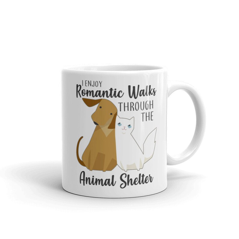 May include: White ceramic coffee mug with a brown dog and white cat illustration. The text reads "I enjoy Romantic Walks through the Animal Shelter."