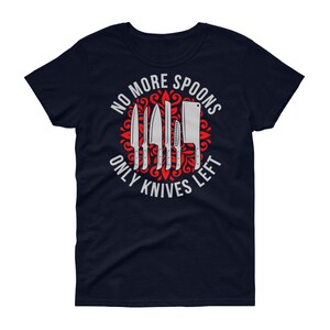 Puede incluir: Camiseta azul marino para mujer con un dise&ntilde;o gr&aacute;fico rojo y blanco. El gr&aacute;fico presenta un c&iacute;rculo con un patr&oacute;n floral rojo y el texto "No More Spoons Only Knives Left" en blanco. El c&iacute;rculo contiene un conjunto de cuchillos plateados.