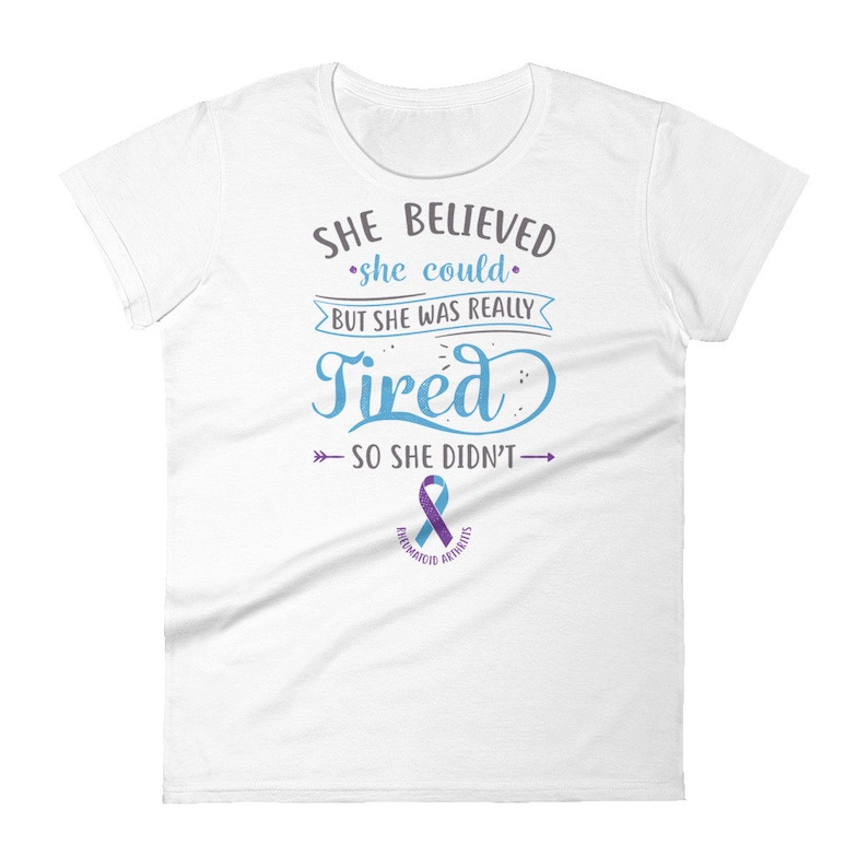 May include: White t-shirt with a blue and gray graphic that reads "SHE BELIEVED she could BUT SHE WAS REALLY Tired SO SHE DIDN'T" with a purple ribbon below the text that says "RHEUMATOID ARTHRITIS".