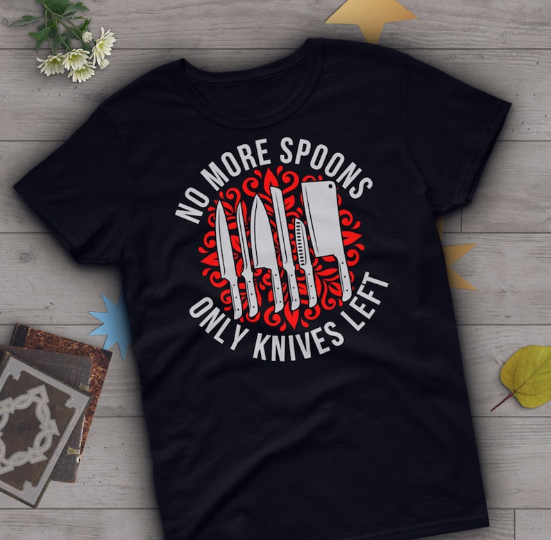 Puede incluir: Camiseta negra con un dise&ntilde;o circular rojo que presenta un conjunto de cuchillos y el texto "No More Spoons Only Knives Left".