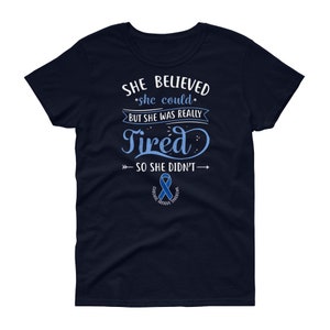 May include: Navy blue women's t-shirt with a white graphic that reads "She believed she could but she was really tired so she didn't."  The graphic also includes a blue ribbon with the text "Chronic Fatigue Syndrome".