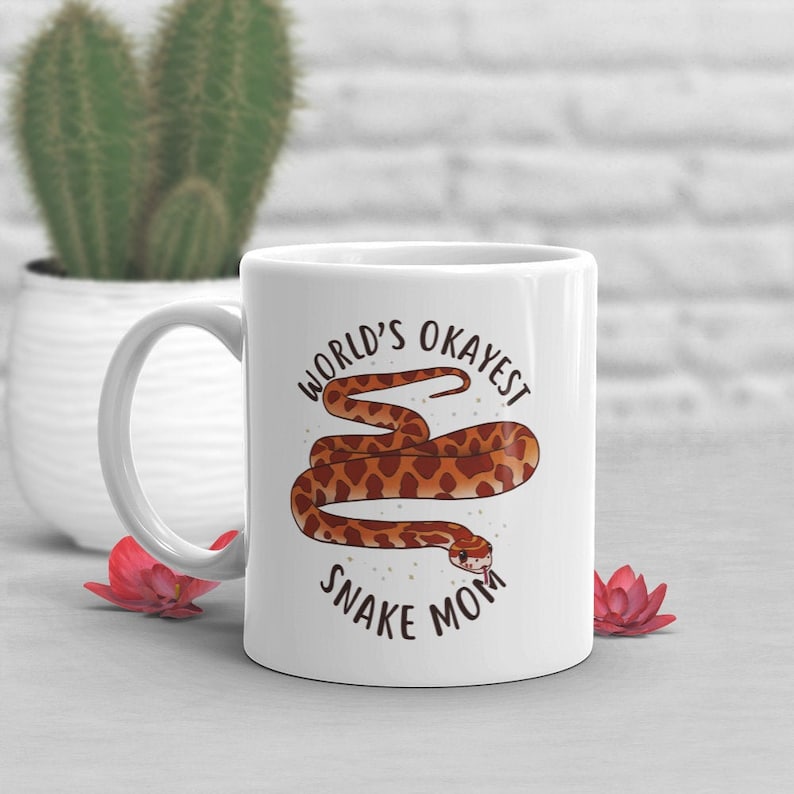 May include: White ceramic coffee mug with a brown snake illustration and the text "World's Okayest Snake Mom".
