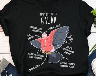 May include: Black t-shirt featuring a detailed diagram of a Galah, labeled "Anatomy of a Galah." The diagram includes humorous labels like "Face Scissors" and "Decibel-Destroying Alert Megaphone," with a pink and gray bird illustration.