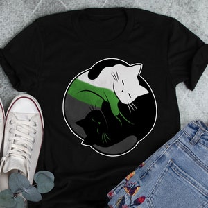 May include: Black t-shirt featuring a yin yang design with two cats. The cats are black and white and are curled up in a yin yang symbol. The background of the shirt is black.