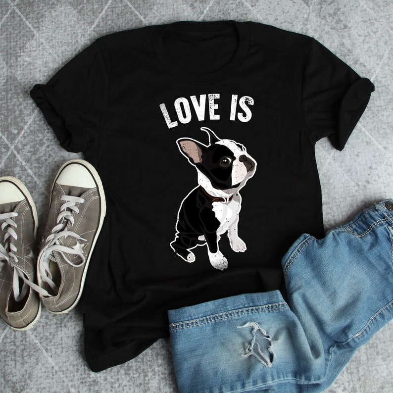 Pode incluir: Camiseta preta com o texto "LOVE IS" e uma ilustra&ccedil;&atilde;o de um Boston Terrier preto e branco.