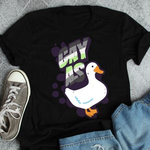 May include: Black t-shirt with a white goose and the text "gay as" in a rainbow color scheme.