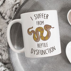 May include: White ceramic mug with a brown and yellow cartoon snake and the text "I suffer from reptile dysfunction".