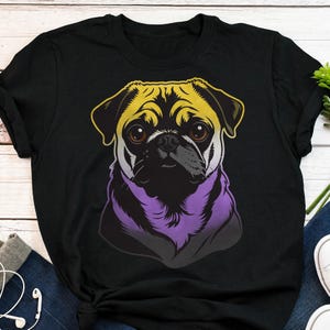 Op de afbeelding: Zwart T-shirt met een gestileerde mopshond-illustratie. De kop van de mopshond is gekleurd met gele, zwarte, paarse en witte accenten. De hond heeft bruine ogen en een zwarte neus. Het T-shirt is een casual item.