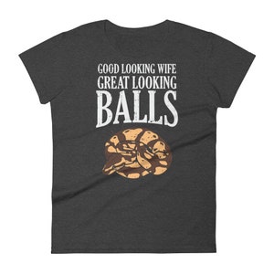 May include: A dark gray t-shirt with the text "GOOD LOOKING WIFE GREAT LOOKING BALLS" in white. A brown and tan snake is curled up below the text.