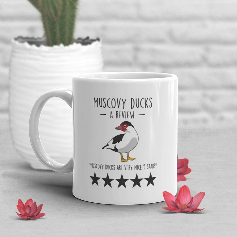 May include: White ceramic mug with a black and white illustration of a Muscovy duck. The mug has the text "Muscovy Ducks - A Review -" and "Muscovy Ducks are very nice 5 stars" with five black stars.