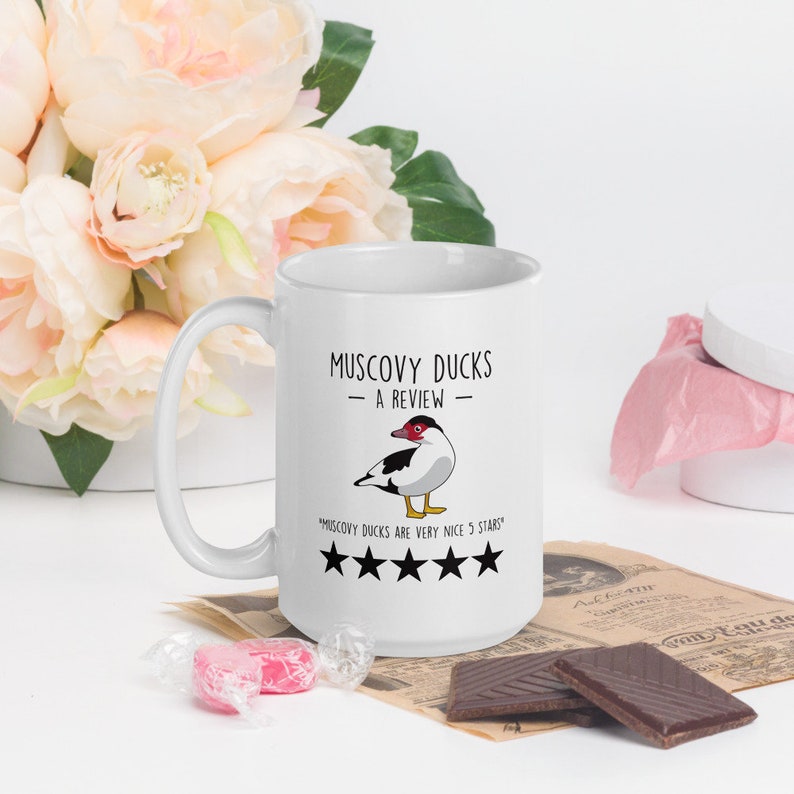 May include: White ceramic coffee mug with a black and white illustration of a Muscovy duck. The text "Muscovy Ducks - A Review" is printed on the mug. Below the duck is a five-star rating with the text "Muscovy Ducks are very nice 5 stars".