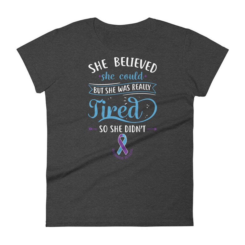 May include: A dark heather grey t-shirt with a blue and white graphic that reads "She believed she could, but she was really tired, so she didn't". A purple awareness ribbon is below the text.