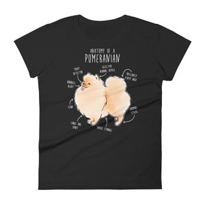 K&ouml;nnte beinhalten: Ein schwarzes T-Shirt mit einer wei&szlig;en Illustration eines Zwergspitz-Hundes. Die Illustration ist mit humorvollen anatomischen Merkmalen beschriftet, wie "Leckerli-Detektor", "Obsz&ouml;n flauschiger Bereich" und "Snack-Lagerung".