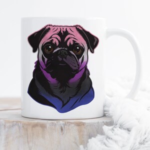 Peut inclure: Mug en céramique blanche avec un portrait de bouledogue carlin stylisé. Le visage du carlin est noir avec des yeux bruns, et le design intègre des couleurs dégradées rose, violet et bleu. La tasse a une anse blanche et est posée sur une surface en bois.