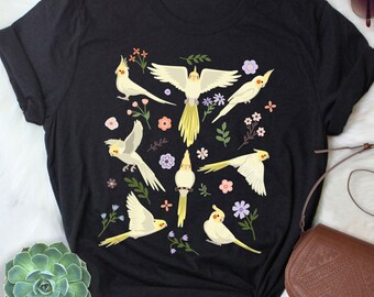 May include: Black t-shirt with a white and yellow graphic print of cockatiels and flowers.