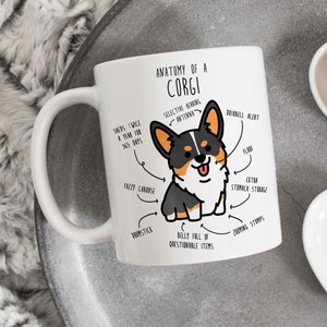 May include: White ceramic mug with a cartoon illustration of a corgi dog. The illustration is labeled with humorous anatomical features, such as "selective hearing antenna", "fuzzy caboose", and "belly full of questionable items".