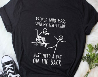 May include: Black t-shirt with a white graphic of a stick figure pushing a person in a wheelchair off a cliff. The text reads "People who mess with my wheelchair just need a pat on the back."