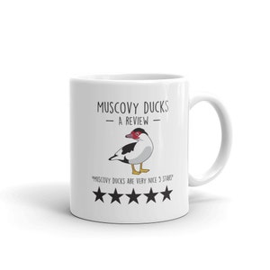 May include: White ceramic mug with a black and white illustration of a Muscovy duck. The text "Muscovy Ducks - A Review -" is printed on the mug. Below the duck is a five-star rating with the text "Muscovy Ducks are very nice 5 stars".