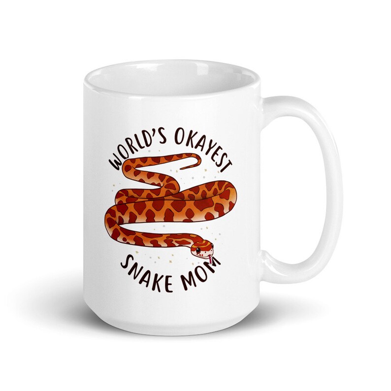 May include: White ceramic mug with a brown and orange snake illustration and the text "World's Okayest Snake Mom".