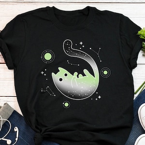 May include: Black t-shirt with a green and white galaxy cat design. The cat is floating in space with stars and planets around it.
