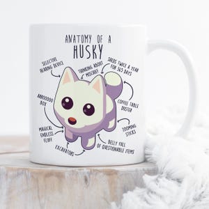 May include: White ceramic mug with a cartoon husky illustration and text that reads "Anatomy of a Husky". The illustration shows the husky with various labels, including "Selective Hearing Device", "Thinking About Mischief", "Sheds Twice a Year for 365 Days", "Arrooooo Box", "Magical Endless Fluff", "Excavators", "Coffee Table Duster", "Zooming Sticks", and "Belly Full of Questionable Items".
