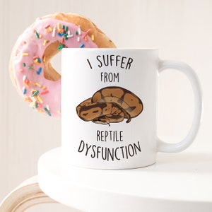 May include: White ceramic mug with a black and brown snake illustration and the text "I suffer from reptile dysfunction".