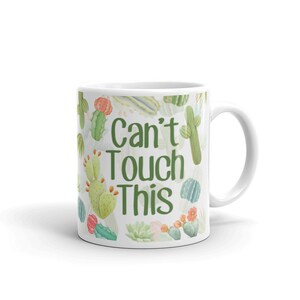 May include: White ceramic mug with a green and white cactus print and the text "Can't Touch This".