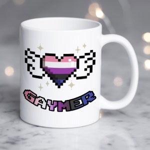 Może przedstawiać: Biały kubek ceramiczny z pikselowym wzorem serca w kolorach flagi dumy biseksualnej i skrzydeł. Tekst "Gaymer" jest napisany na banerze pod sercem.