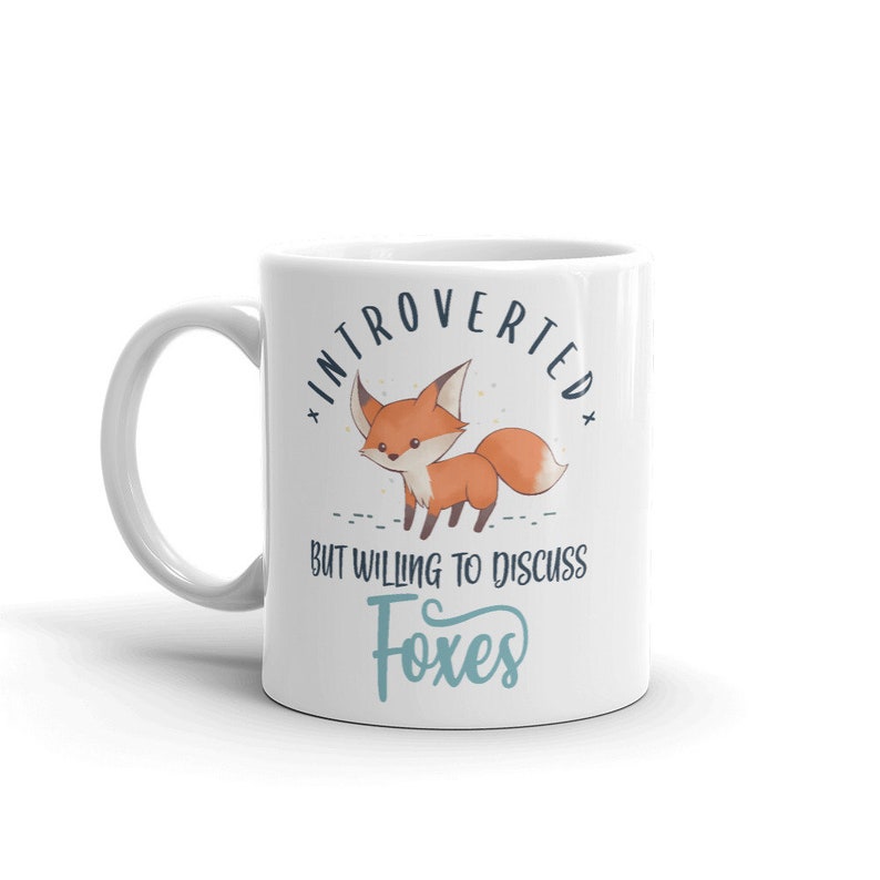 May include: White ceramic mug featuring a cartoon fox and the text "Introverted but willing to discuss foxes".
