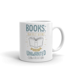 Puede incluir: Taza de cer&aacute;mica blanca con el texto "BOOKS: YOUR BEST DEFENSE AGAINST UNWANTED CONVERSATION" en verde azulado y dorado. El dise&ntilde;o incluye una ilustraci&oacute;n de un libro abierto. Un regalo perfecto para los amantes de los libros.