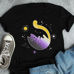Peut inclure: T-shirt noir avec un motif de chat violet, jaune et noir. Le chat est entouré d'étoiles et de planètes.