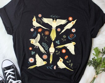 May include: Black t-shirt with a white and yellow illustration of cockatiels and floral designs.
