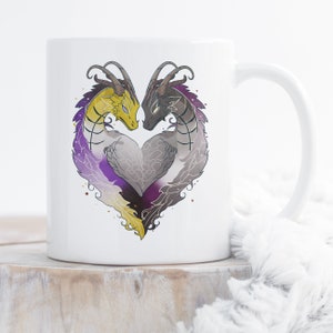 May include: White ceramic mug with a design of two dragons forming a heart shape. The dragons are gold, purple, and black. The heart is filled with a purple, yellow, and black gradient.