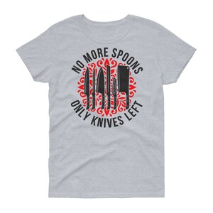 Puede incluir: Camiseta gris con un dise&ntilde;o gr&aacute;fico en negro y rojo. El gr&aacute;fico presenta un c&iacute;rculo con un dise&ntilde;o floral rojo y el texto "No More Spoons Only Knives Left" en negro. Hay seis cuchillos negros dentro del c&iacute;rculo.