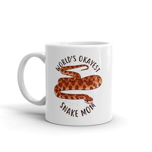 May include: White ceramic mug with a brown and orange snake illustration and the text "World's Okayest Snake Mom".