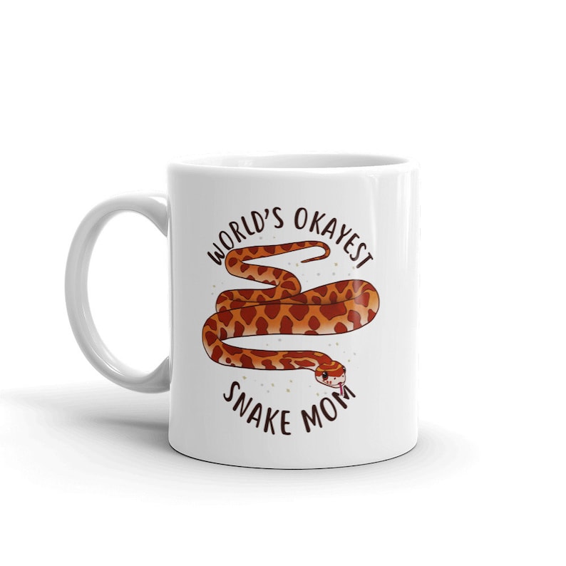 May include: White ceramic mug with a brown and orange snake illustration and the text "World's Okayest Snake Mom".